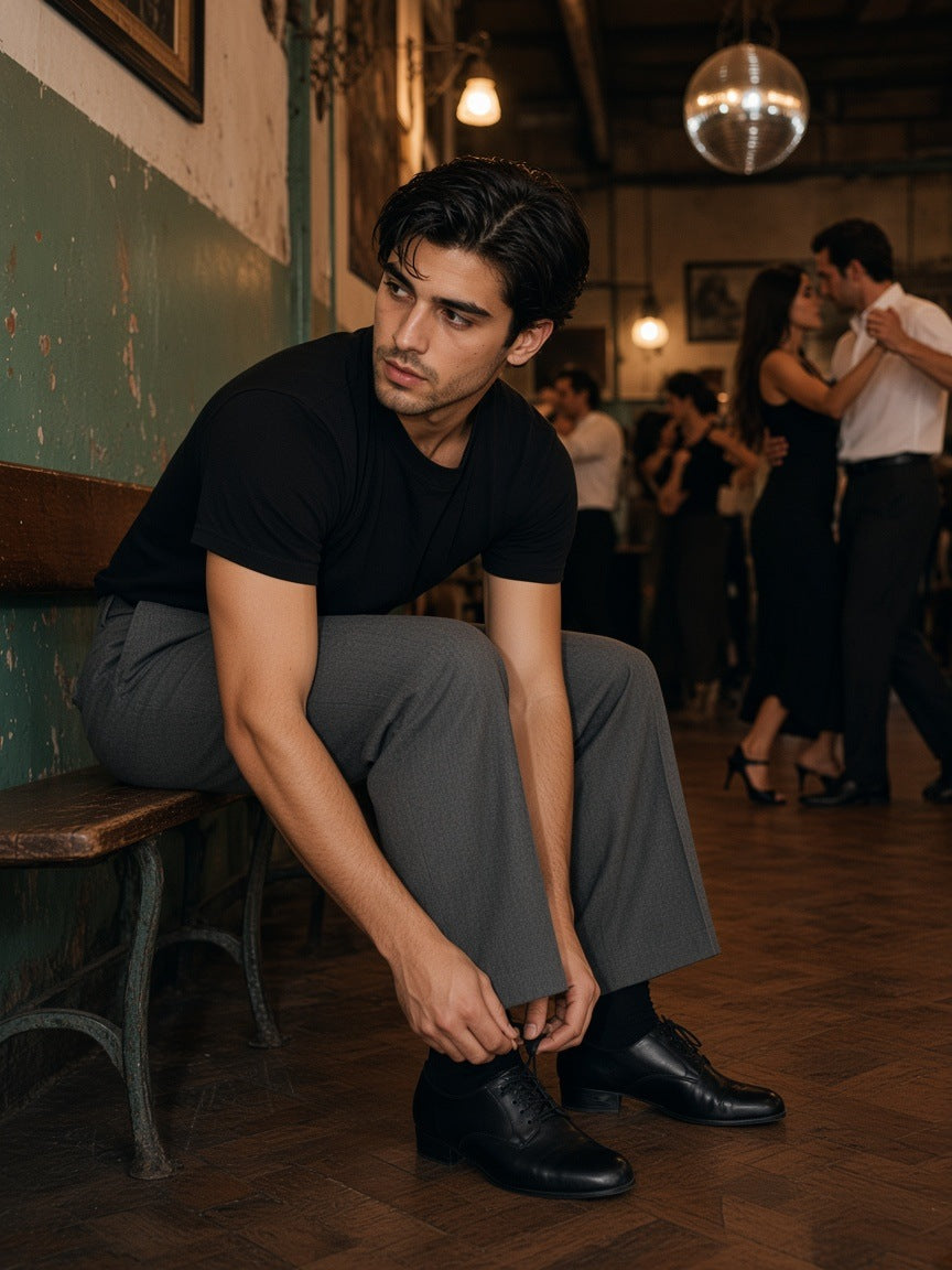Man in the Men's Heavyweight Boxy T-Shirt in Black with grey wool trousers, tying his dance shoe in a Buenos Aires tango hall