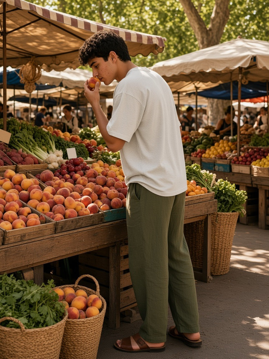 Man in the Men's Heavyweight Drop Shoulder T-Shirt in Oat Gray with olive linen trousers, choosing peaches at a Provençal market