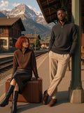 Two people in the Quarter-Zip Pullover Sweatshirt in Brown and Dark Gray, one seated on a suitcase and one leaning on a pillar, on a Swiss mountain railway platform at golden hour