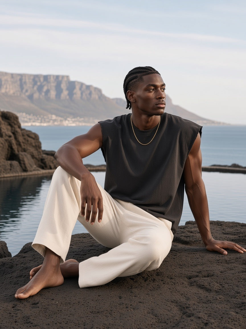 Man in the Raw Edge Boxy Sleeveless Top in Black, on dark stone by the sea in Cape Town in the morning