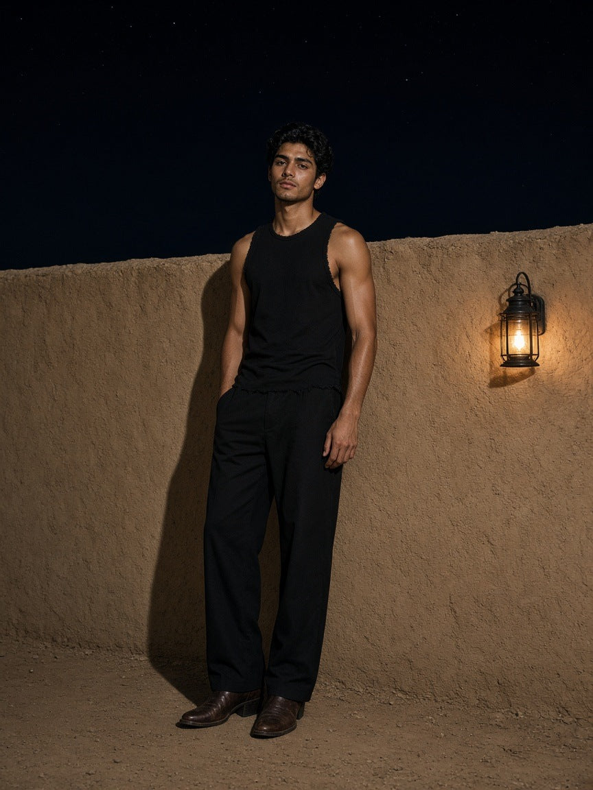 Man in the Marcel Afters Raw Edge Cotton Tank Top in Black against an adobe wall outside Marfa, Texas at night