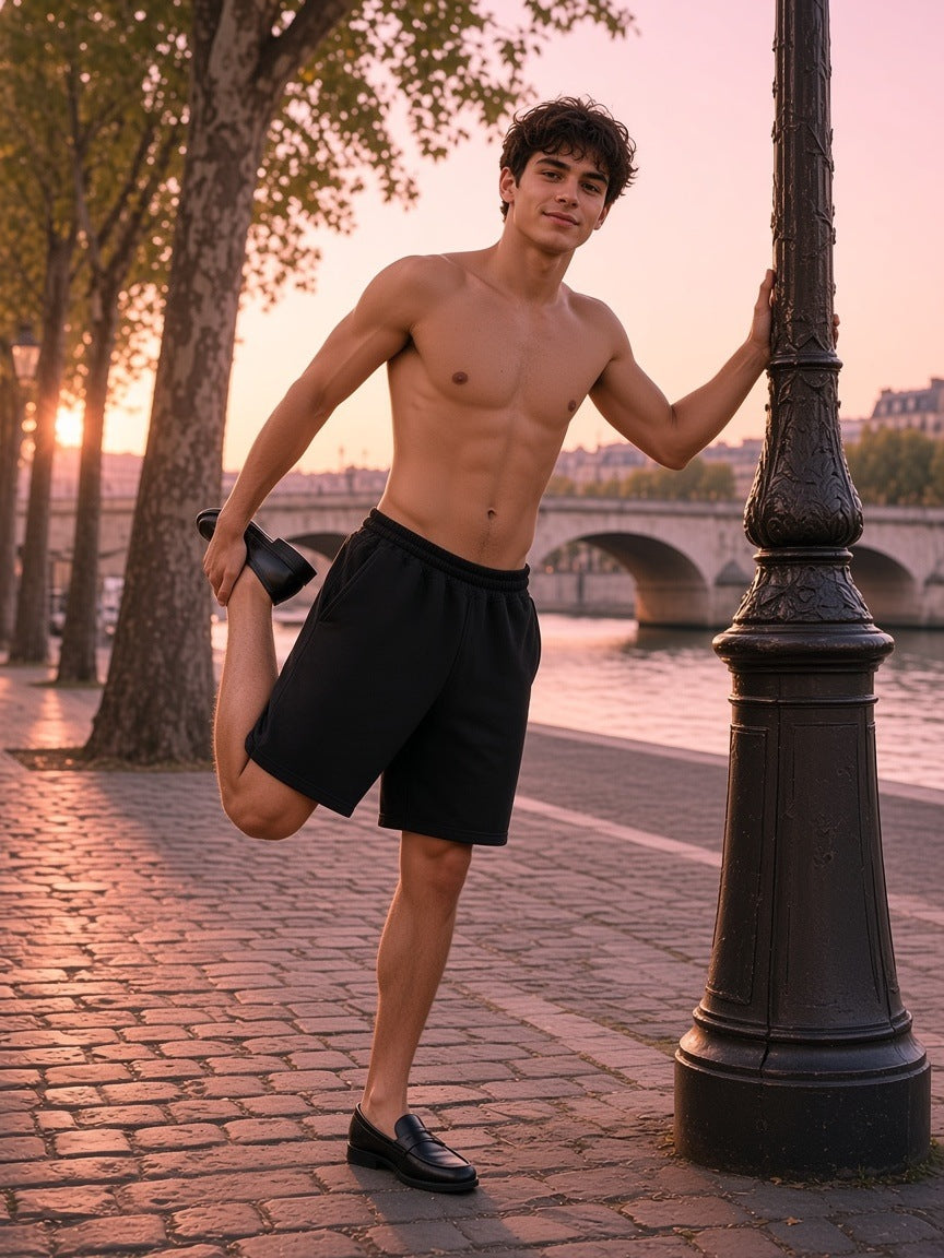 Man in the Raw Edge Fleece Shorts in Black, shirtless, stretching by a lamp post on a Seine quay at sunrise