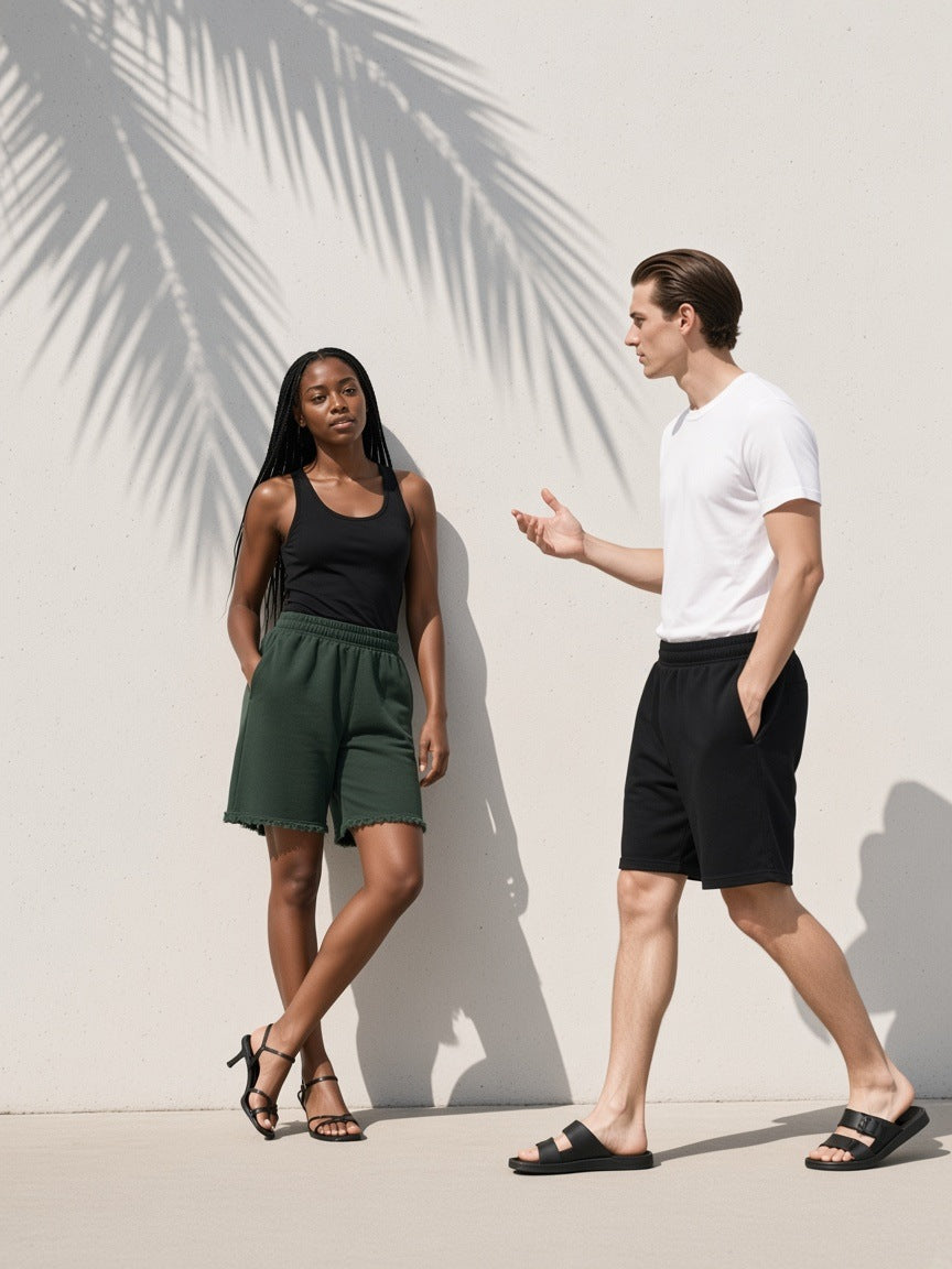 Two people in the Raw Edge Fleece Shorts in Dark Green and Black, walking past a concrete wall with palm shadow in Los Angeles by day