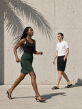 Two people in the Raw Edge Fleece Shorts in Dark Green and Black, walking past a concrete wall with palm shadow in Los Angeles