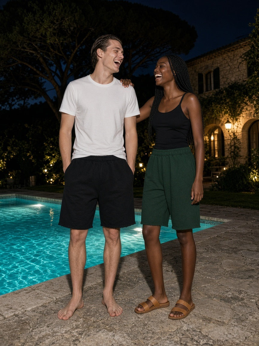 Two people in the Marcel Afters Raw Edge Fleece Shorts in Black and Dark Green by a Cap Ferrat villa pool at night