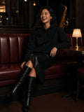 Woman in the Relaxed Pullover Hoodie in Black with a black leather midi skirt and knee boots, laughing in a jazz club booth at night