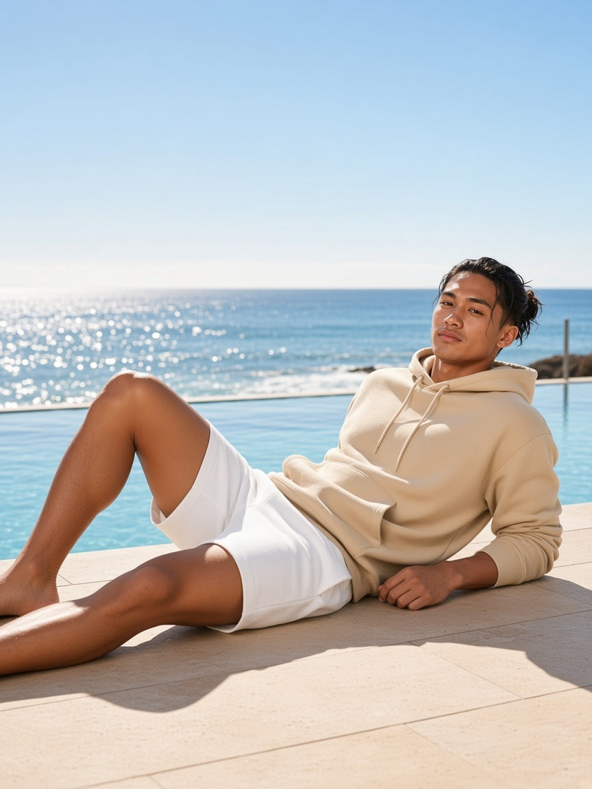 Man in the Relaxed Pullover Hoodie in Khaki with white shorts, barefoot by an ocean pool in Sydney in the morning