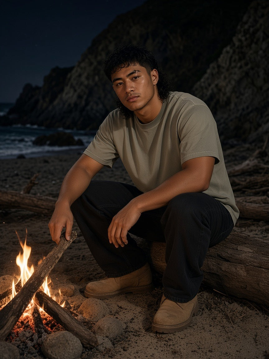 Man in the Reverse Dyed Loose Cotton T-Shirt in Green low by a driftwood fire on a rocky Big Sur cove at night