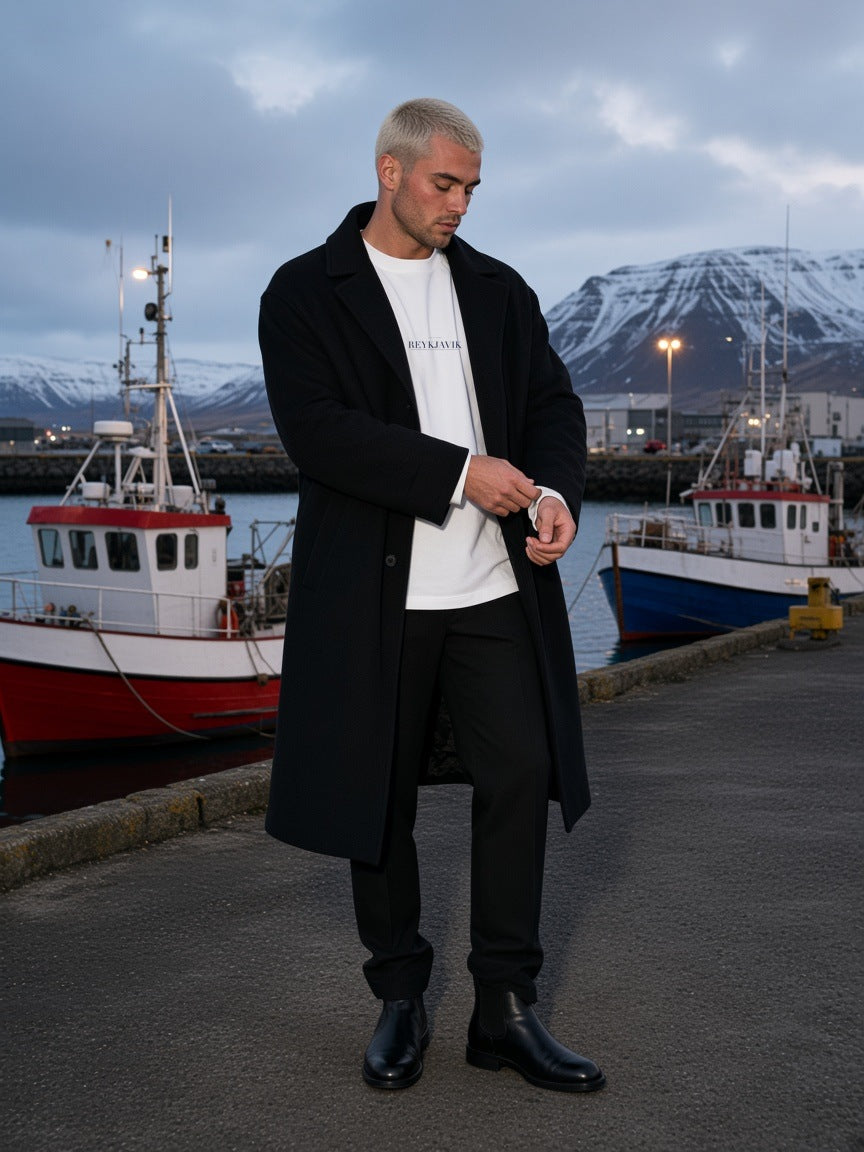 Man in the Reykjavik Heavyweight Drop Shoulder T-Shirt in White with the navy Reykjavik city plate, on the snowy harbour edge of Reykjavik under the northern lights at night
