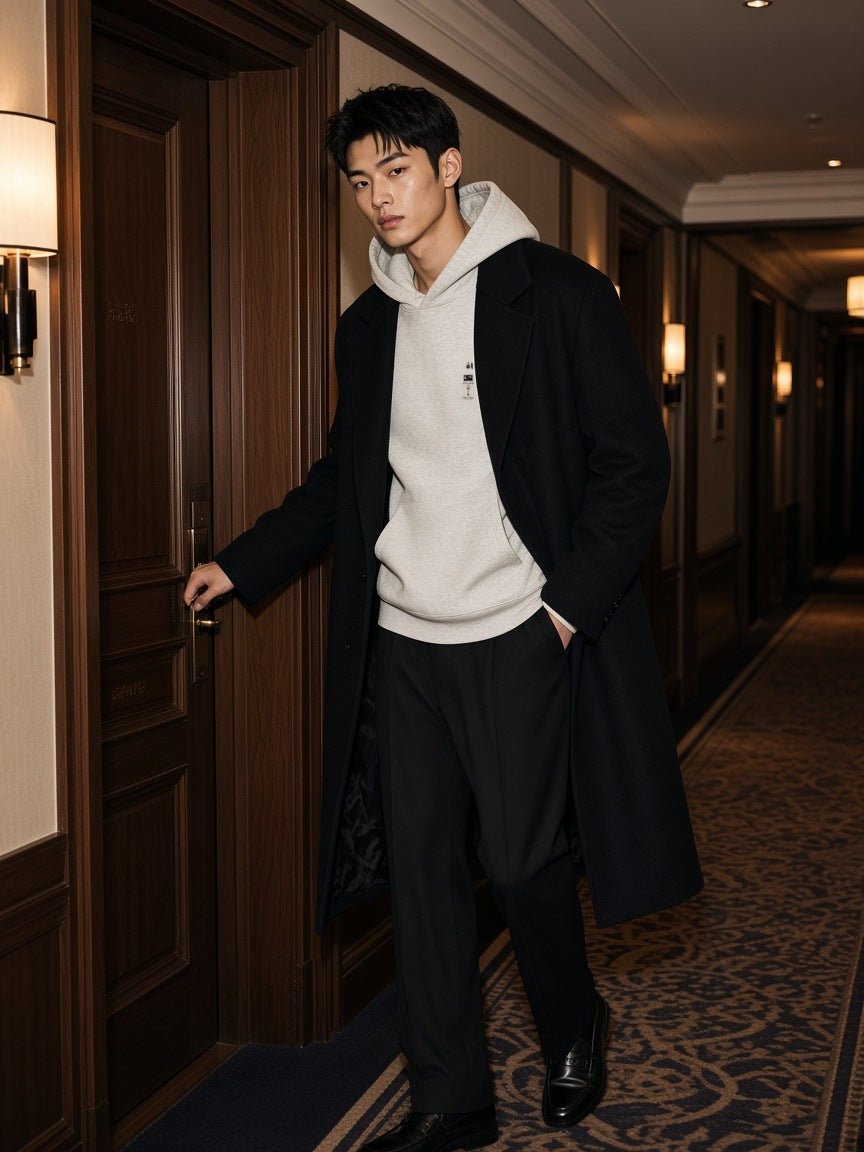 Man in the Room 237 hoodie in Oat Gray under a long dark coat at a hotel room door at night