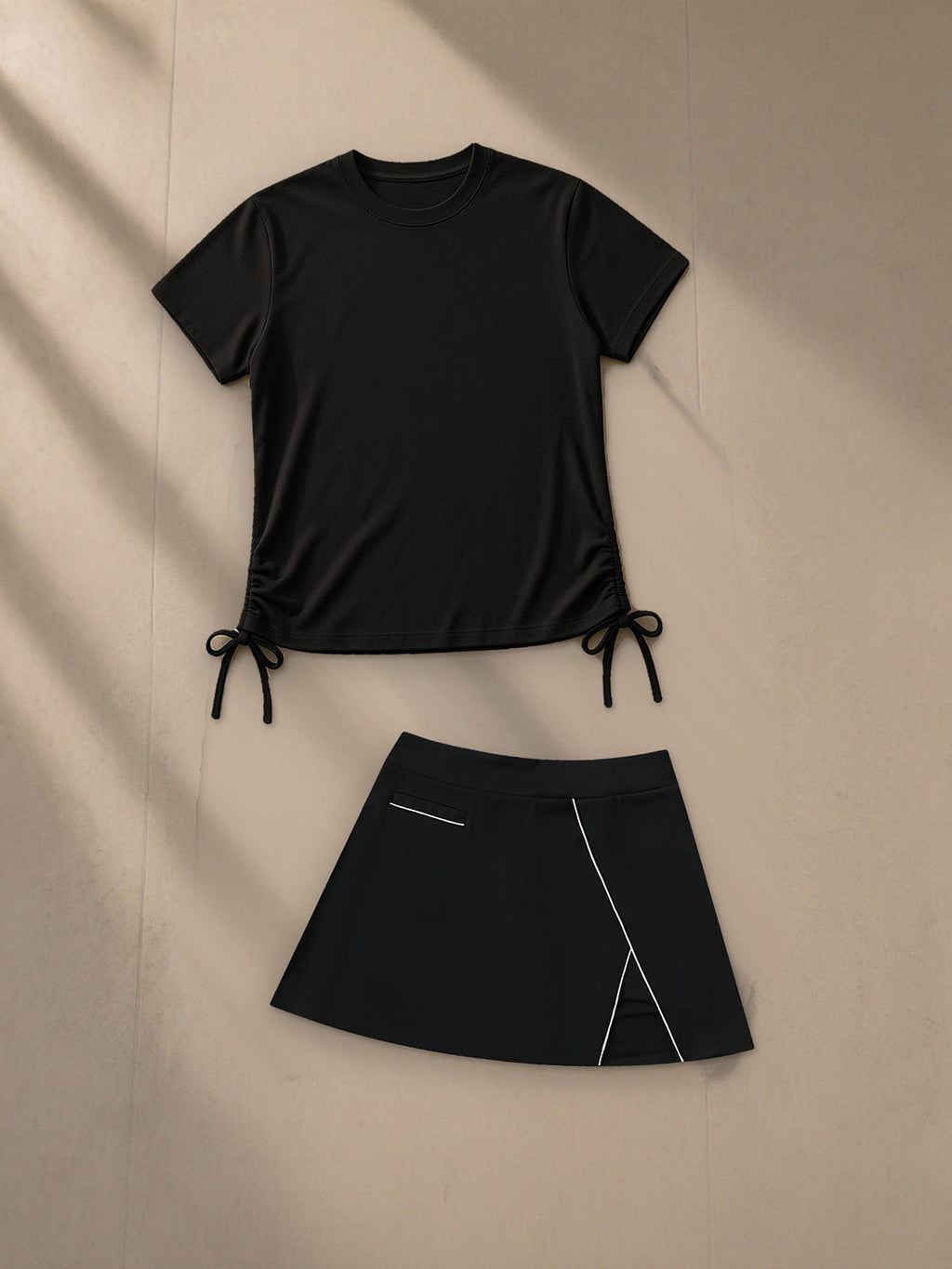 Essential Drawstring T-Shirt and High-Waist Pocketed A-Line Skirt in Black, top and bottom laid flat together on pale limestone