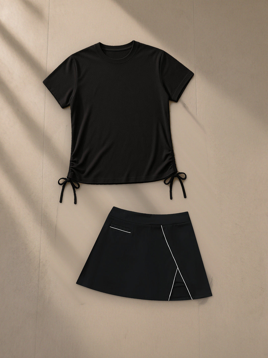 Essential Drawstring T-Shirt and High-Waist Pocketed A-Line Skirt in Black, top and bottom laid flat together on pale limestone