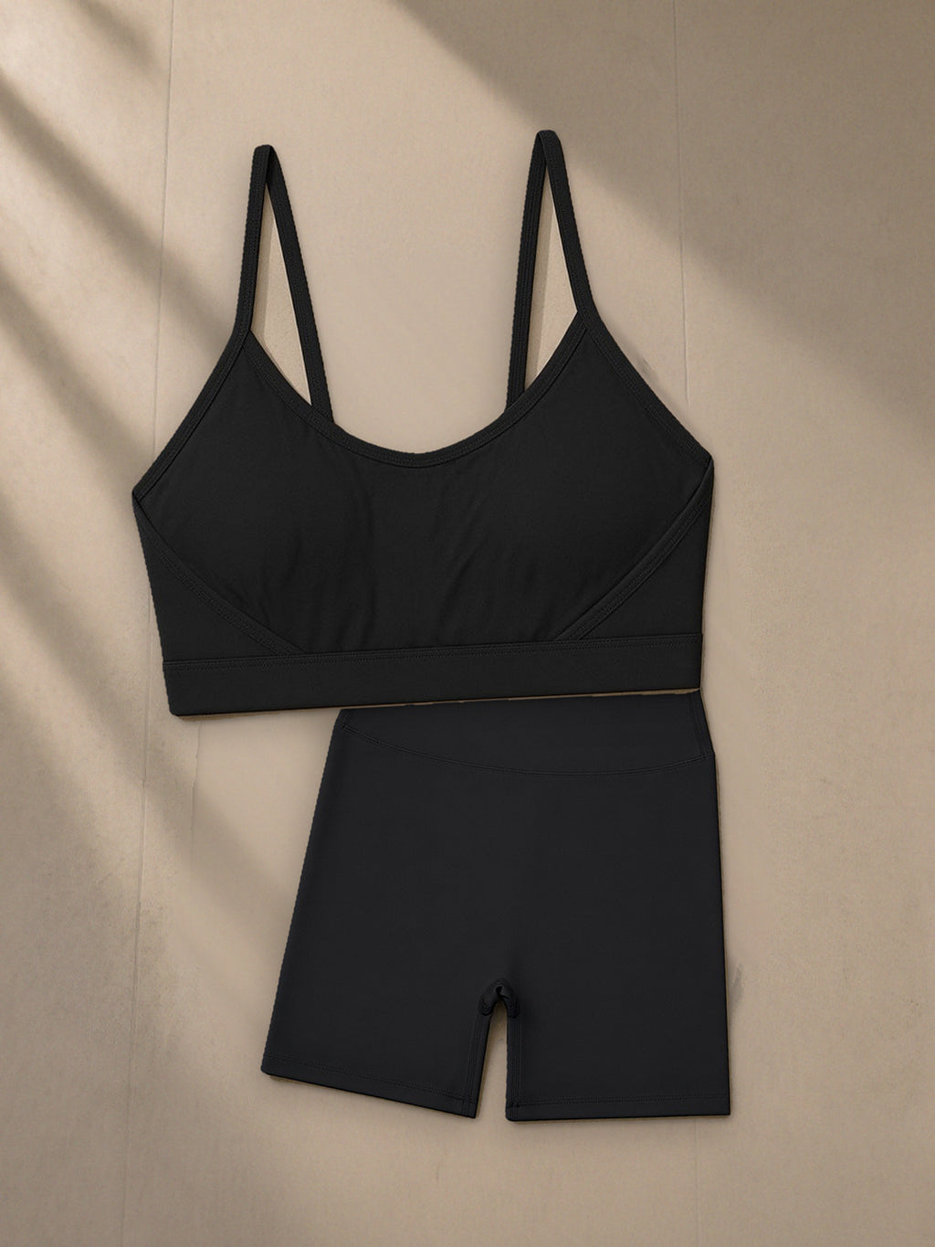 Women's Tight Yoga Sports Bra + High Waisted Yoga Biker Shorts Set in Black, top and bottom laid flat together on pale limestone