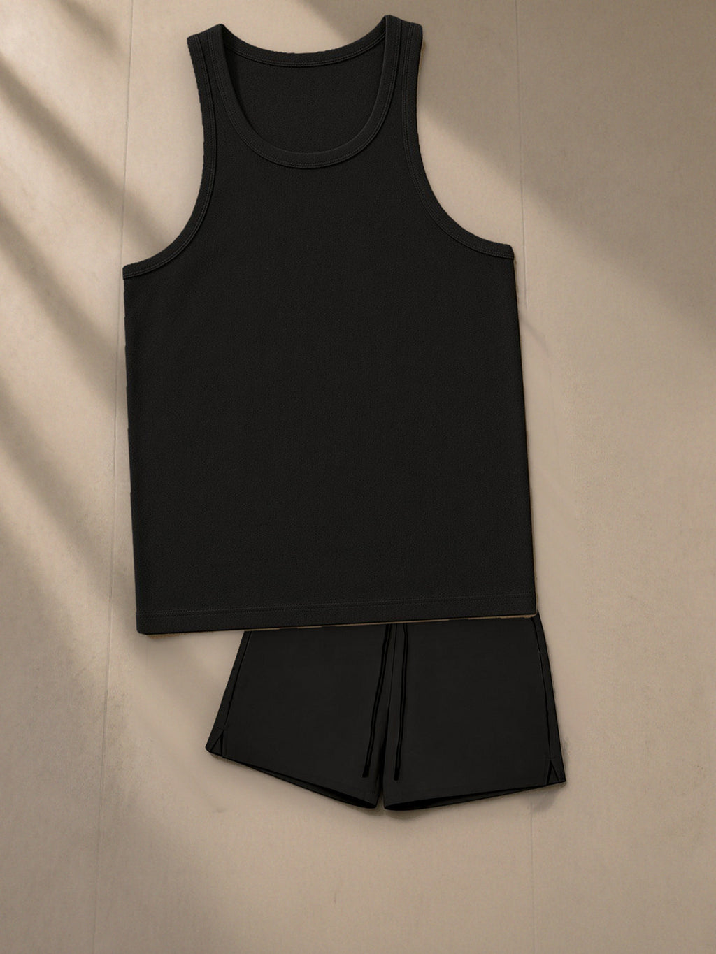 Men's Essential Performance Tank Top + Pocketed Compression-Lined Performance Shorts Set in Black, top and bottom laid flat together on pale limestone