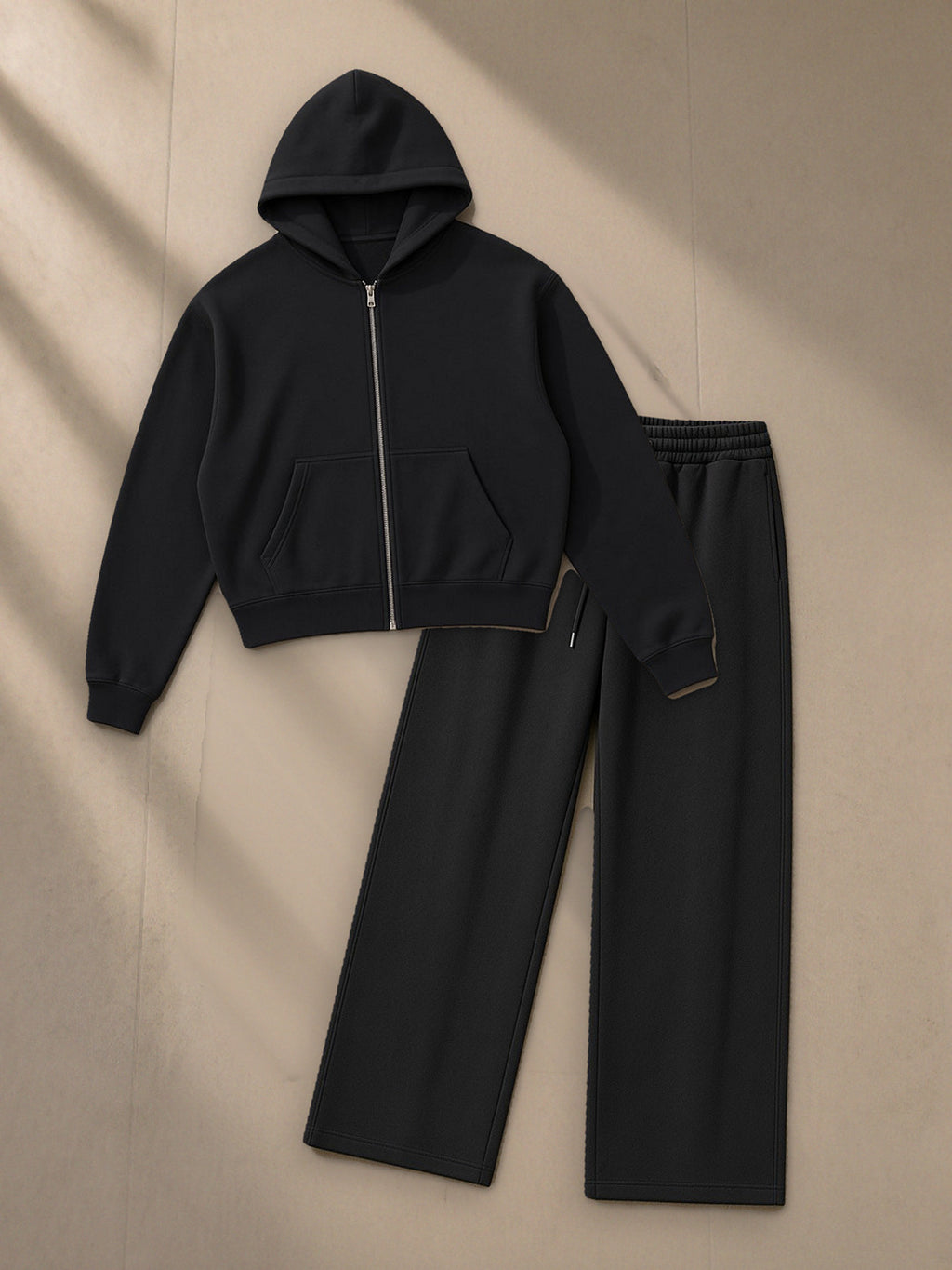 Women's Essential Cropped Zip-Up Hoodie + Essential Straight-Leg Sweatpants Set in Black, top and bottom laid flat together on pale limestone