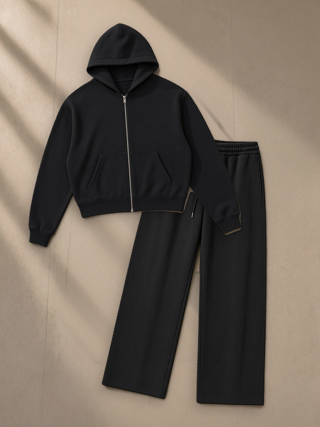 Women's Essential Cropped Zip-Up Hoodie + Essential Straight-Leg Sweatpants Set in Black, top and bottom laid flat together on pale limestone