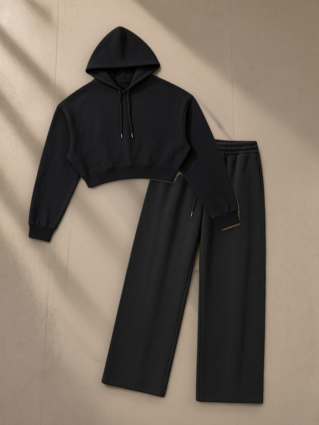 Women's Essential Cropped Hoodie + Essential Straight-Leg Sweatpants Set in Black, top and bottom laid flat together on pale limestone