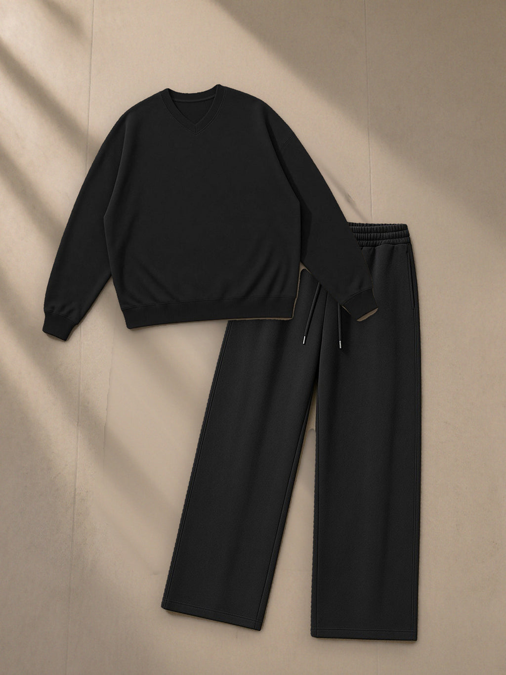 Oversized V-Neck Sweatshirt + Essential Straight-Leg Sweatpants Set in Black, top and bottom laid flat together on pale limestone