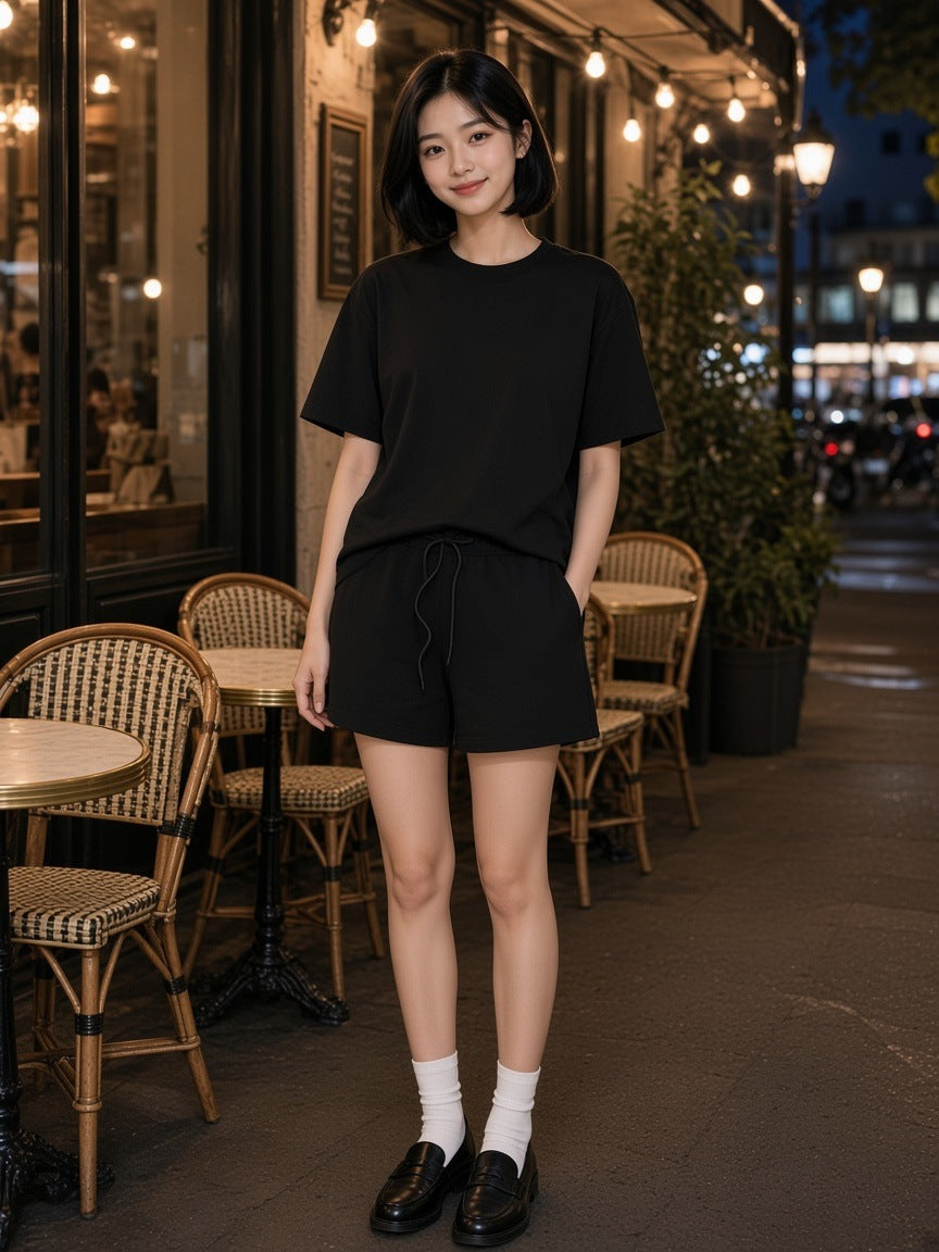 Woman in the Black Earth Tone set, heavyweight tee and loose cotton shorts, at a Paris cafe terrace at night