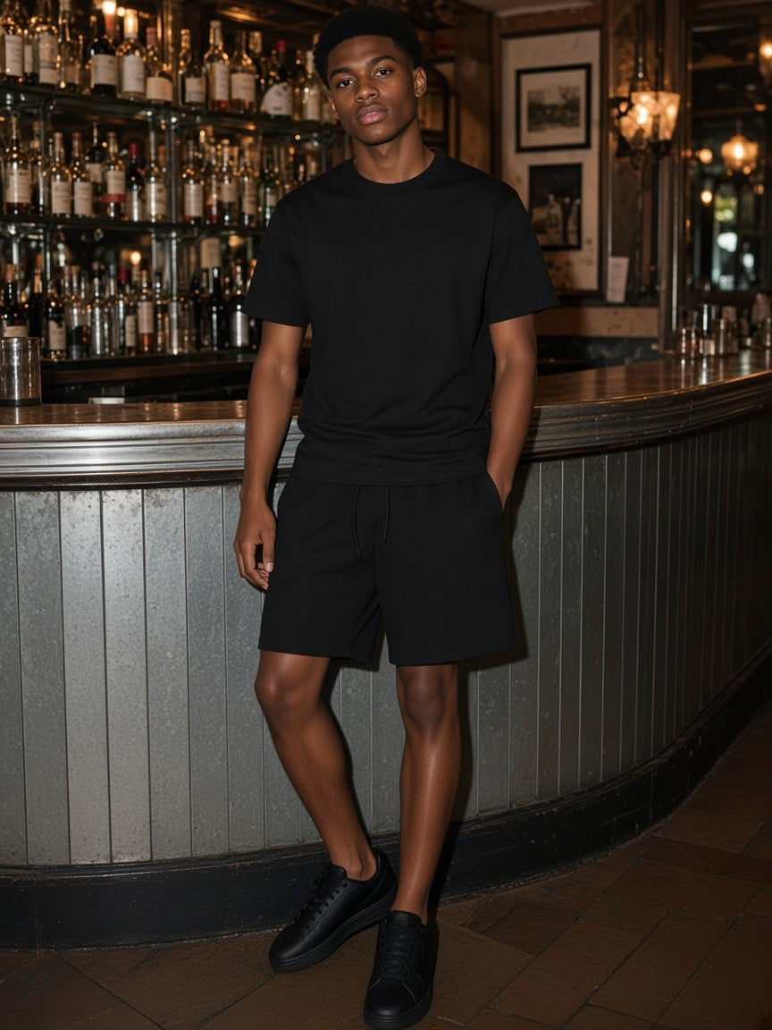 Man in the Black Earth Tone set, heavyweight tee and loose cotton shorts, at a zinc bistro bar in Paris
