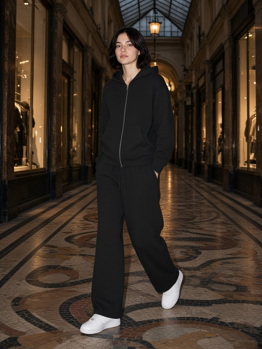 Woman in the Black Waffle set, full zip hoodie and barrel leg pants, in a covered Paris passage at night