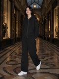 Woman in the Black Waffle set, full zip hoodie and barrel leg pants, in a covered Paris passage at night