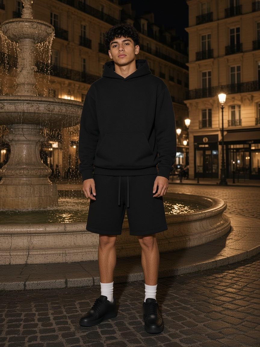 Man in the Black Fleece set, heavyweight hoodie and fleece shorts, by a fountain in a Paris square at night