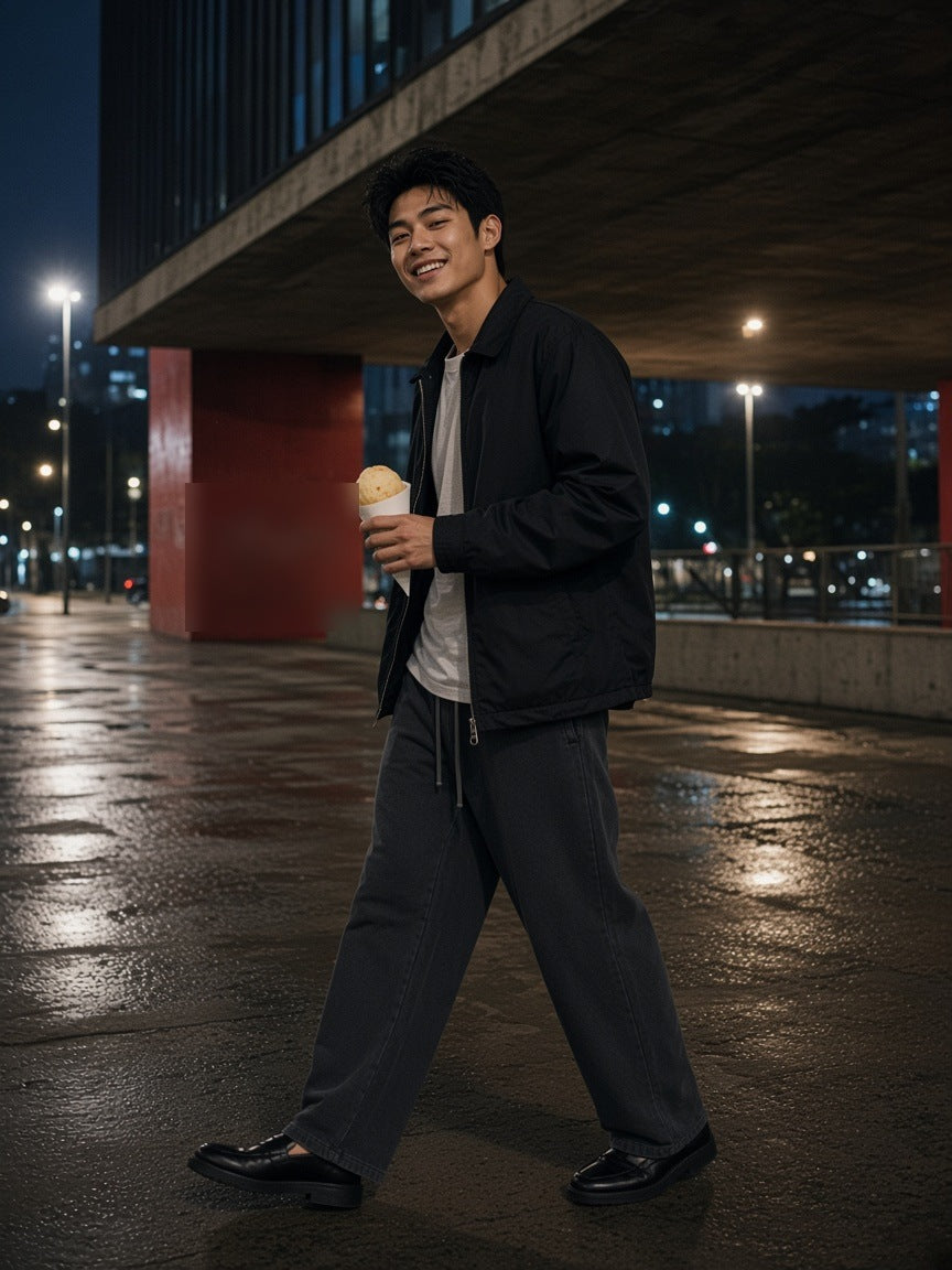 Man in the Snow Wash Heavyweight Sweatpants in Black with a nylon overshirt and loafers, walking under a Brutalist concrete overhang in São Paulo at night