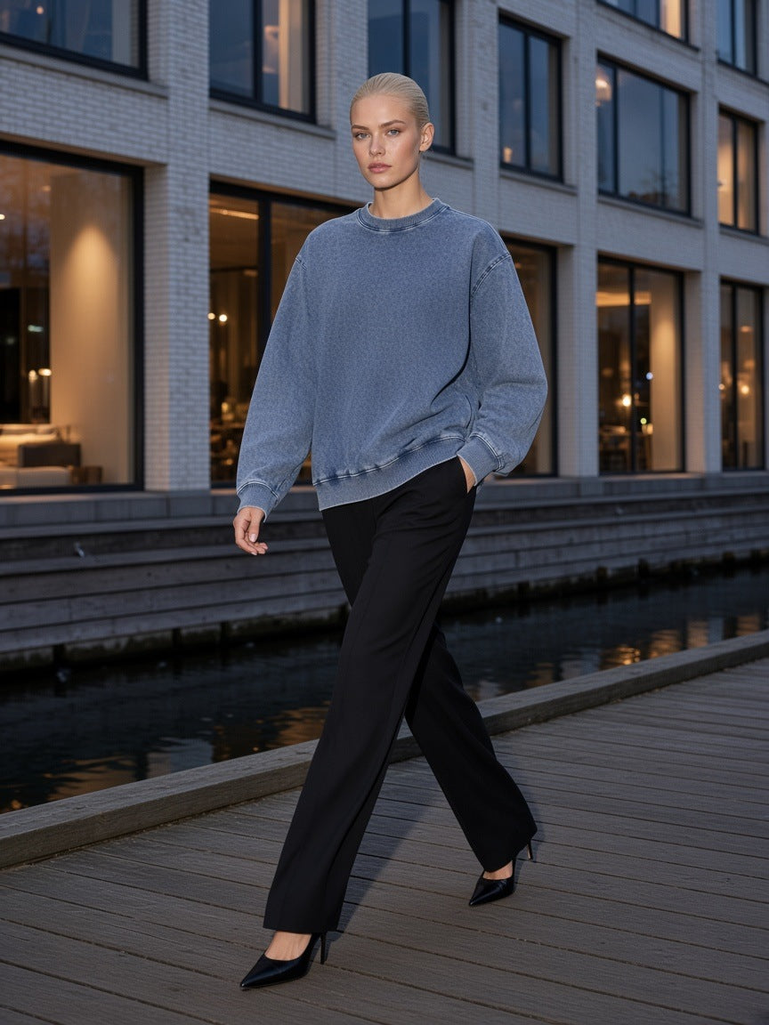Woman in the Marcel Afters Snow Wash Oversized Crewneck Sweatshirt in Light Blue, on a harbourside boardwalk at blue hour in Copenhagen