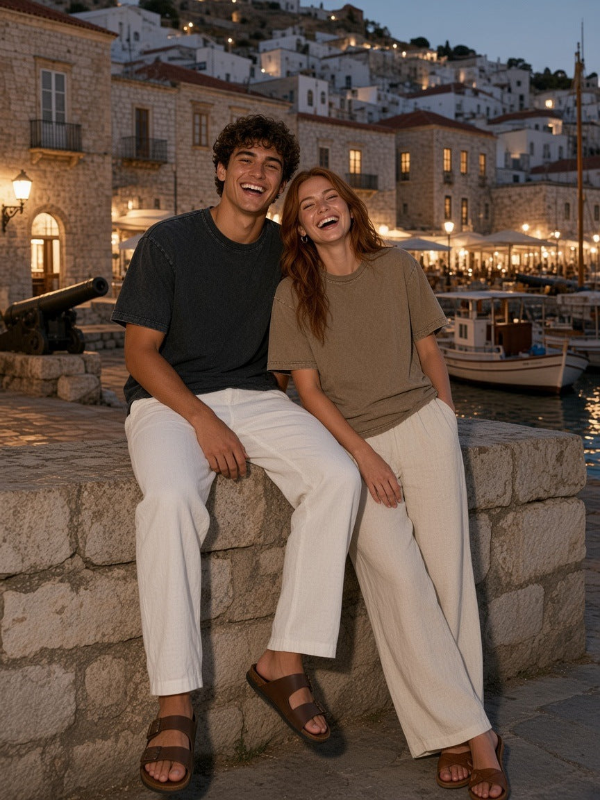 Two people in the Marcel Afters Snow Washed Heavyweight Oversize T-Shirt in Black and Coffee on the Hydra harbour at night