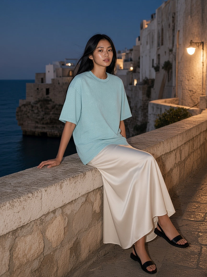 Woman in the Marcel Afters Snow Washed Oversized Cotton T-Shirt in Water Blue at a villa pool edge at a resort in Bali at blue hour