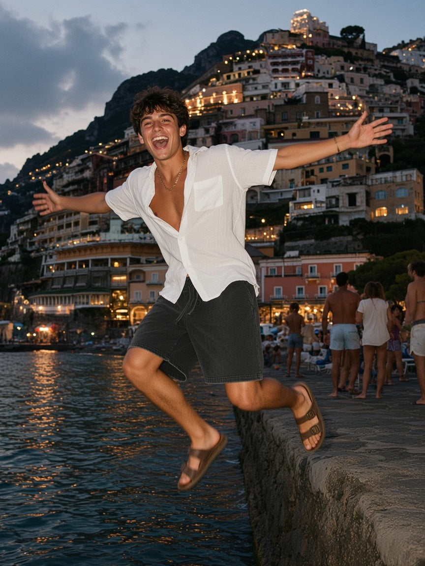 Man in the Snow Washed Raw Hem Shorts in Black, leaping off a Positano jetty at dusk