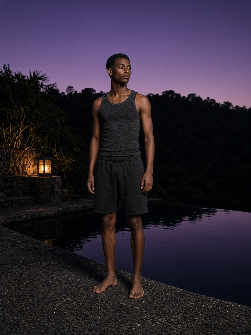 Man in the Marcel Afters Snow Washed Tank Top in Black at a volcanic stone infinity pool at a resort in Bali at dusk