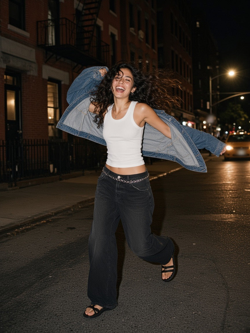 Woman in the Snow Washed Tank Top in White with baggy black jeans, spinning with a denim jacket in a Lower East Side street in Manhattan at 2am