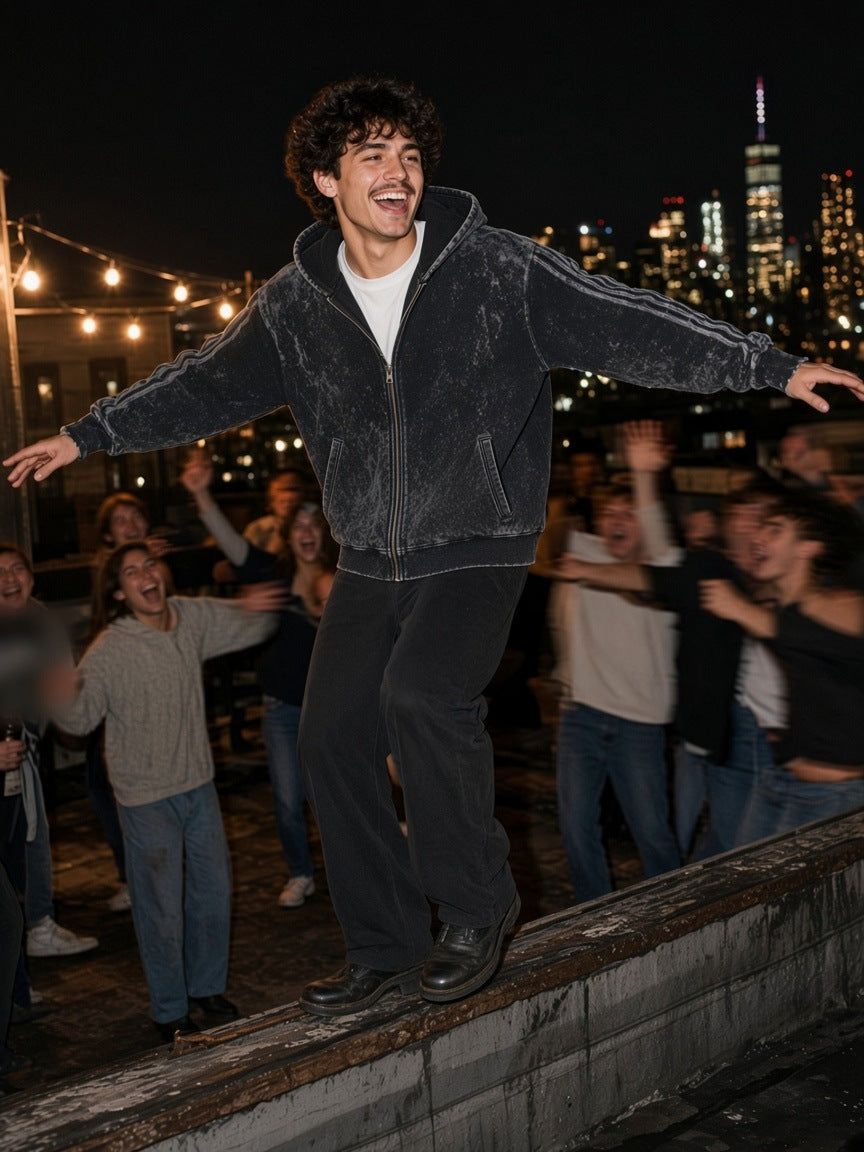 Man in the Snow Washed Tape Raw Edge Zip Hoodie in Black, balancing on a Brooklyn rooftop ledge at 3am