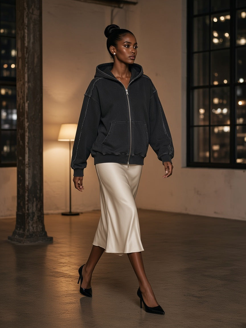 Woman in the Marcel Afters Snow Washed Tape Raw Edge Zip Hoodie in Black with an ivory satin skirt in a hotel loft suite in New York at night