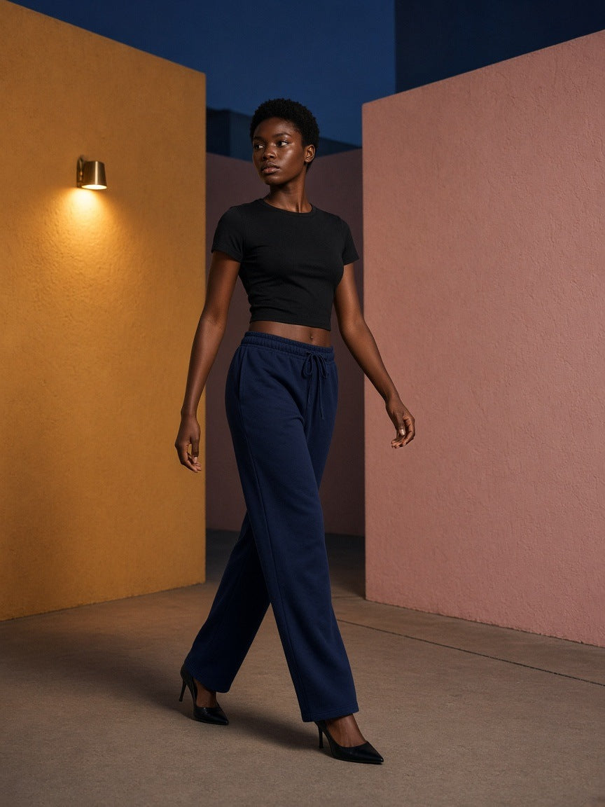Woman in the Marcel Afters Solid Color Straight-Leg Sweatpants in Navy Blue walking through an ochre and pink courtyard in Mexico City at blue hour