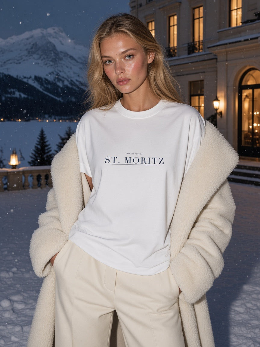 Woman in the St. Moritz Heavyweight Drop Shoulder T-Shirt in White on a snowy palace hotel terrace in St. Moritz at night