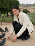 Woman in the Stand Collar Jacket in Beige crouching to feed pigeons in the Tuileries garden in Paris