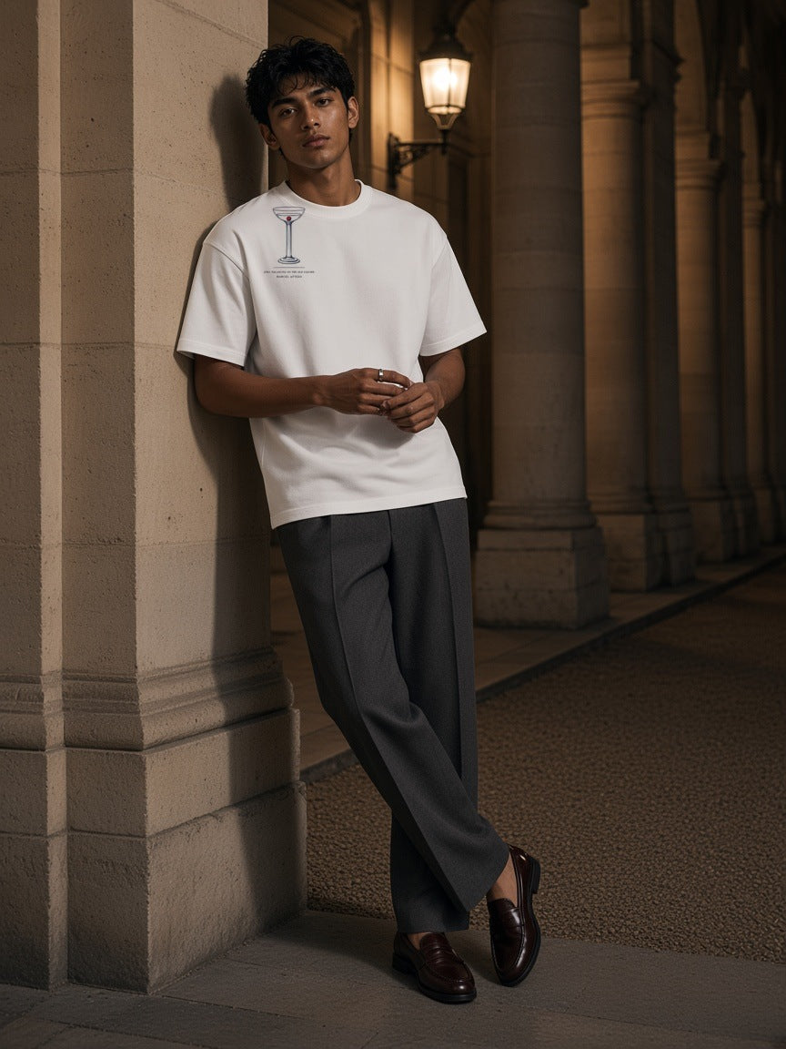 Man in the Still Balancing On The Old Column Heavyweight Drop Shoulder T-Shirt in White leaning on a stone column in the Palais-Royal arcades in Paris at night