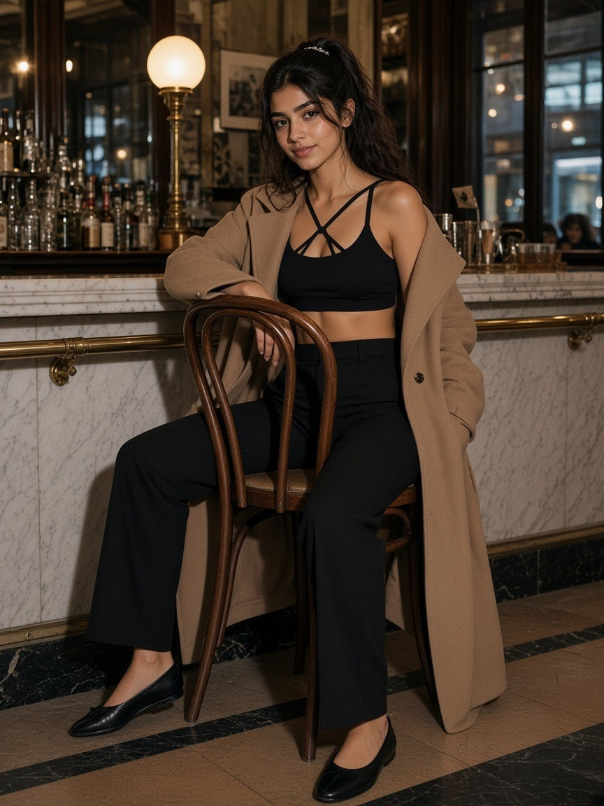 Woman in the Strappy Criss Cross Yoga Sports Bra in Black under a camel coat at the marble bar of a Viennese café at night