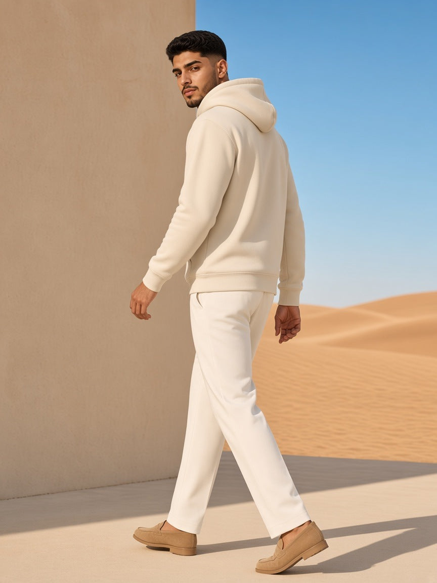 Man in the Streetwear Fleece Hoodie in Cream Apricot with white trousers, against a sand-toned villa wall in Dubai in the morning