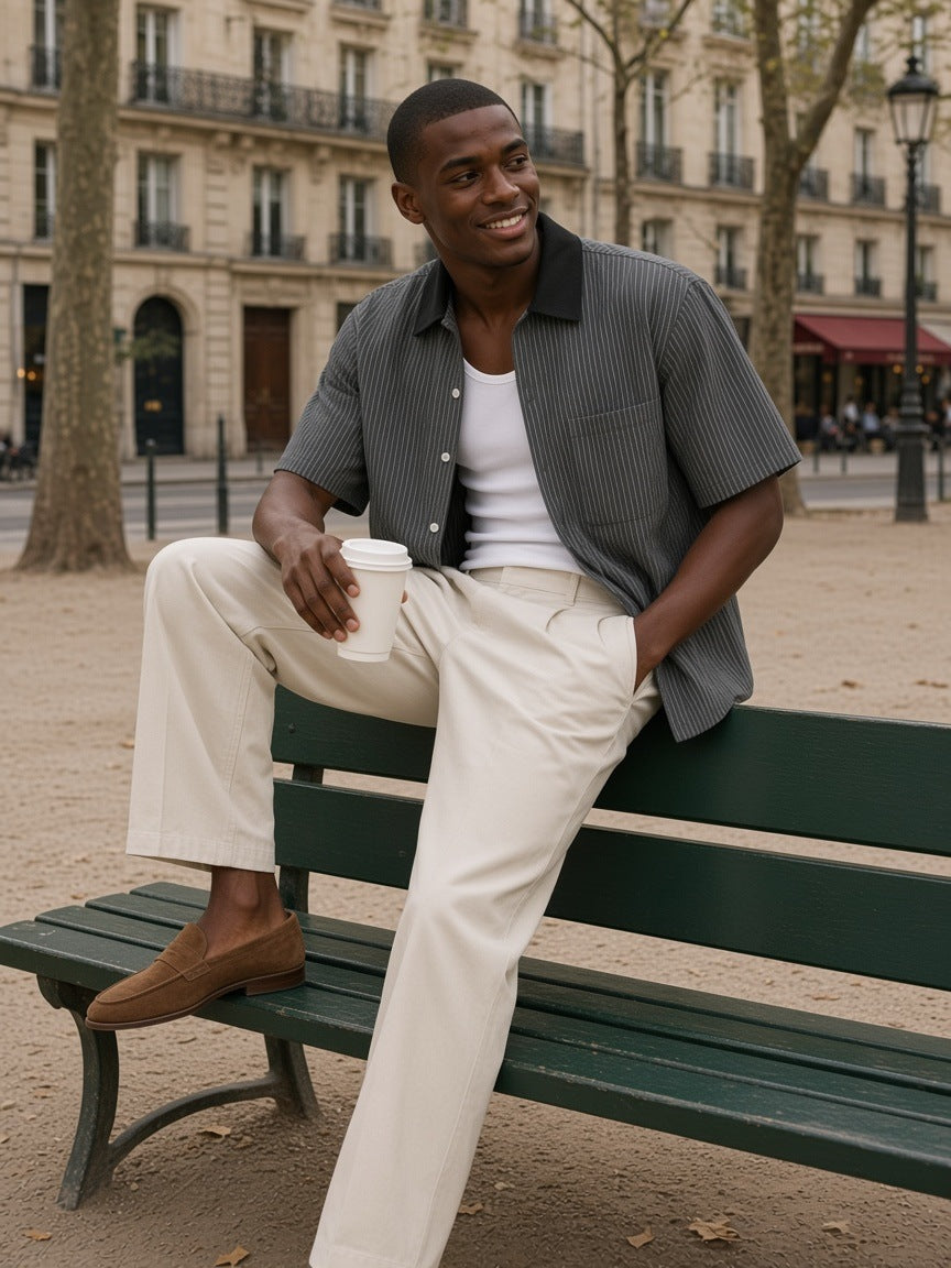 Man in the Striped Boxy Contrast Collar Shirt in Dark Gray, worn open over a white tank, sitting on a Paris park bench in the morning