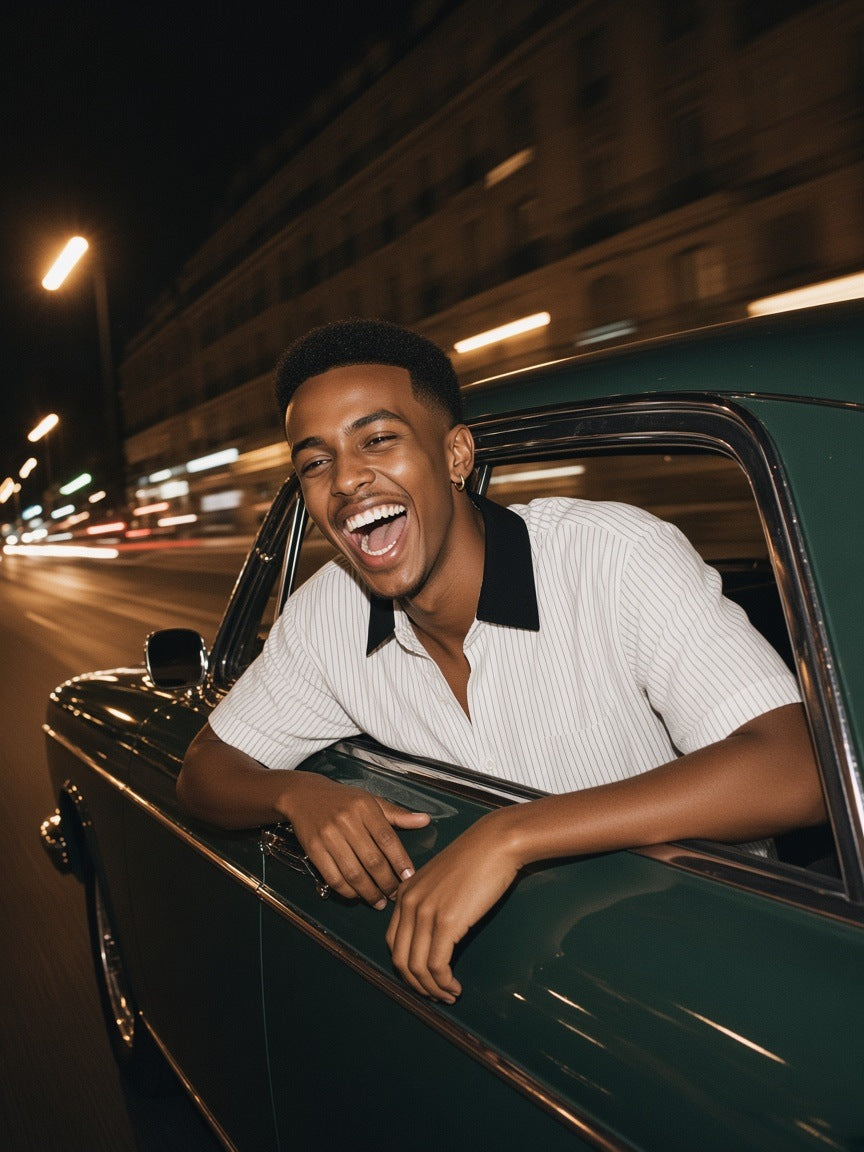 Man in the Striped Boxy Contrast Collar Shirt in White, leaning out of a vintage car window on a Paris boulevard at night