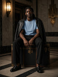 Man in the Sueded Cotton T-Shirt in Light Blue seated on a steamer trunk in an Art Deco lobby in Mexico City at night
