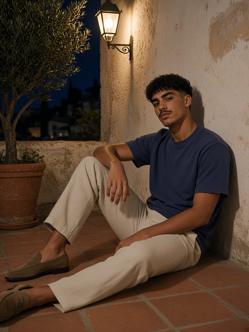 Man in the Sun Fade Raw Edge T-Shirt in Navy Blue seated against a whitewashed wall on a Mallorca finca terrace at night