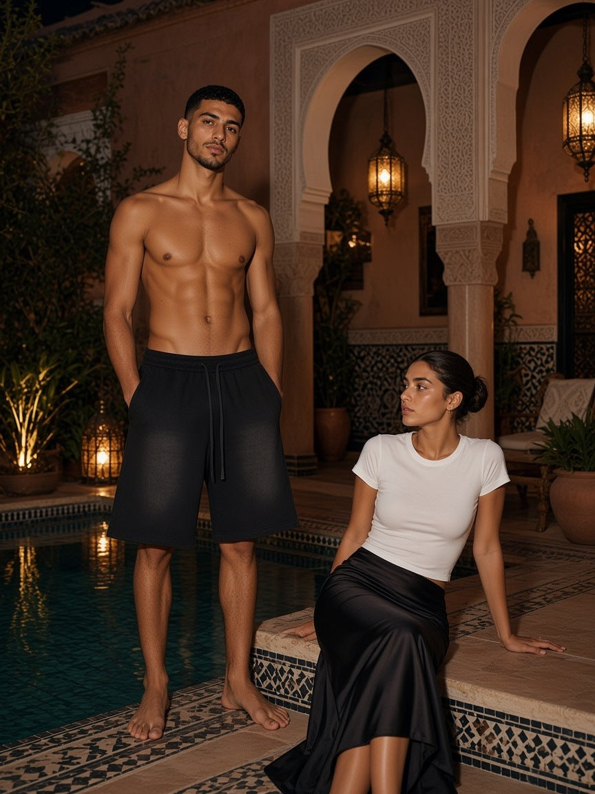 Two people in Marcel Afters, the Sunfade Raw Edge Shorts in Black, beside a riad pool in lantern light in Marrakech