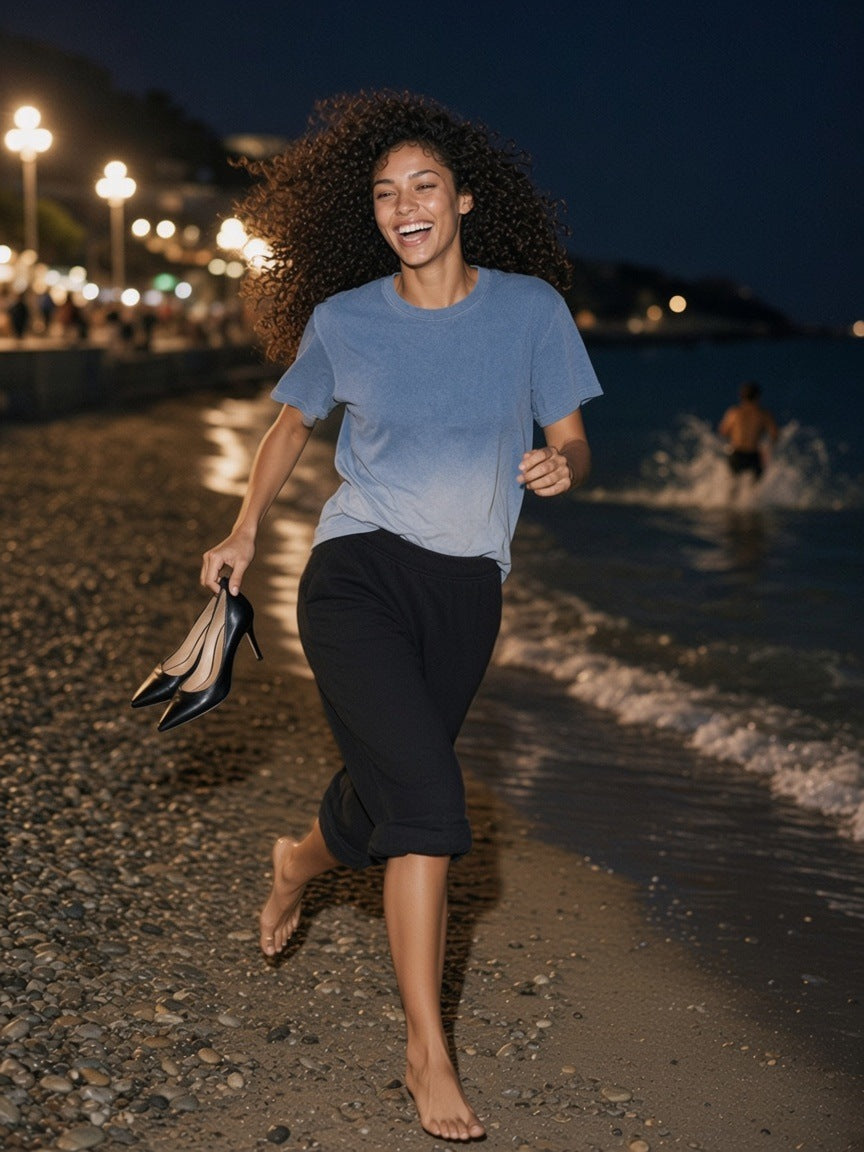 Woman in the Sunfade Vintage Washed T-Shirt in Blue, running barefoot along the beach in Nice at 3am