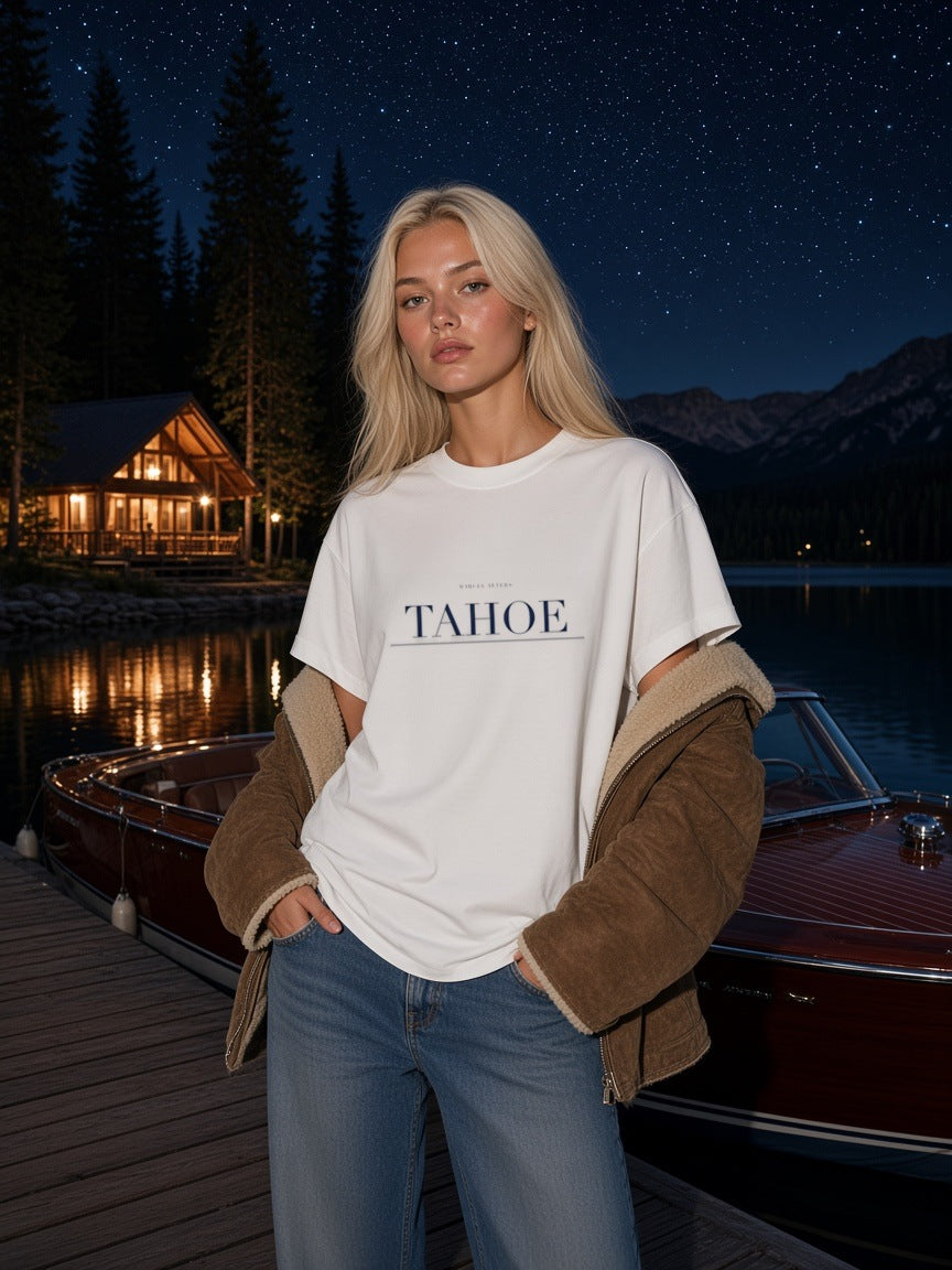 Woman in the Tahoe Heavyweight Drop Shoulder T-Shirt in White with the navy Tahoe city plate, on a lake dock at Lake Tahoe at night