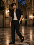 Man in a black Tencel jacquard shirt over a white tank in a glass-roofed arcade at night